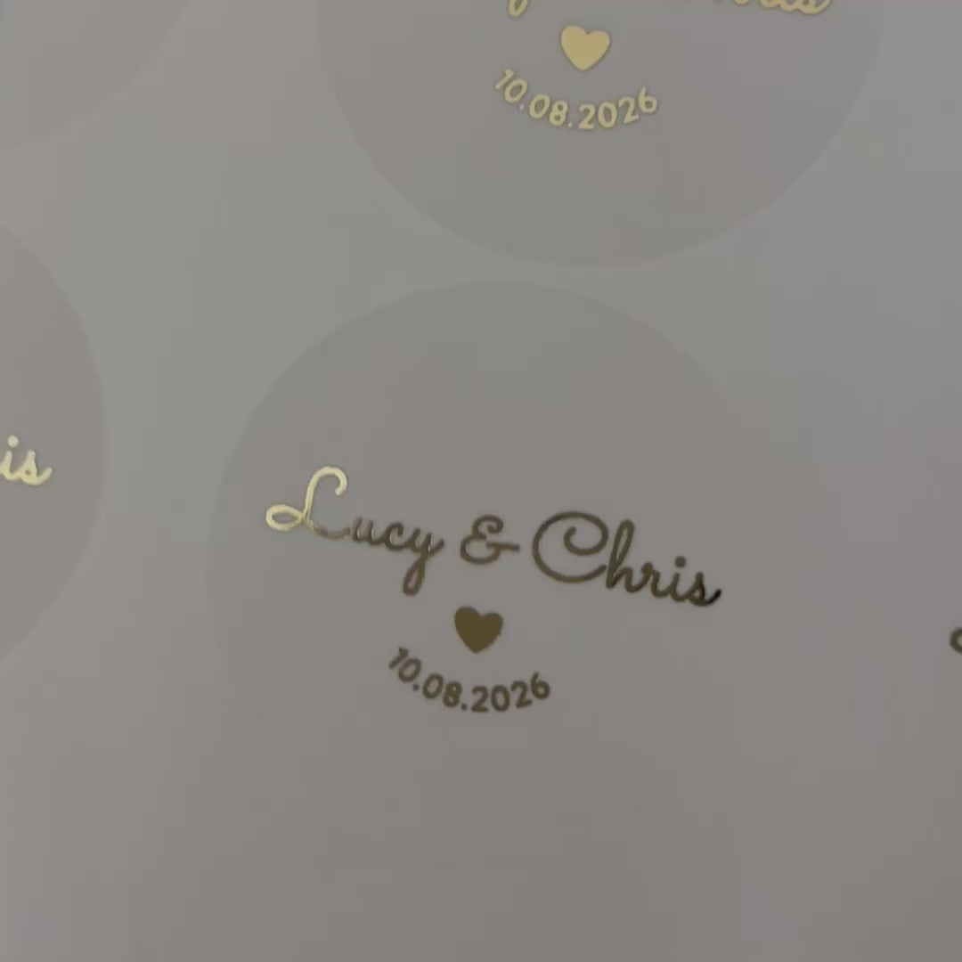 Load video: Personalised Wedding Stickers with names and date and a heart moving to show the high shine gold foil finish